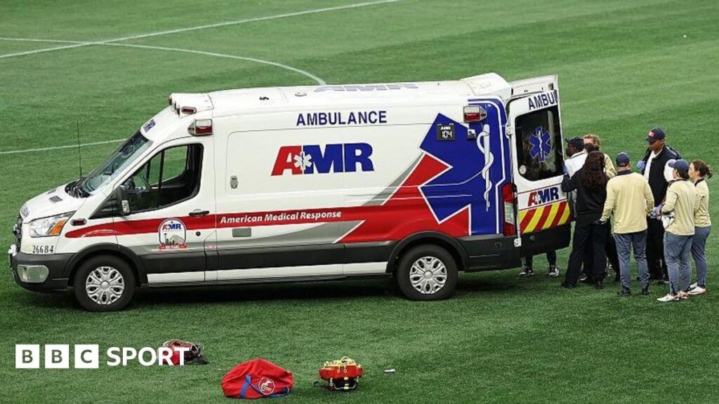 An ambulance on the pitch of a National Women's Soccer League match with people stood behind the vehicle